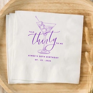 May include: A white paper napkin featuring a purple line drawing of a martini glass with olives. The text reads "TALK thirty TO ME" in a script font, followed by "AIMEE'S 30TH BIRTHDAY" and the date "09 . 23 . 2026" in a clean sans-serif font.