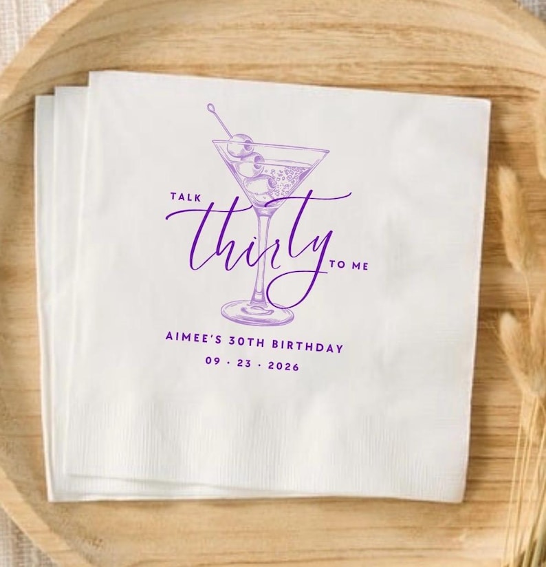 May include: A white paper napkin featuring a purple line drawing of a martini glass with olives. The text reads "TALK thirty TO ME" in a script font, followed by "AIMEE'S 30TH BIRTHDAY" and the date "09 . 23 . 2026" in a clean sans-serif font.
