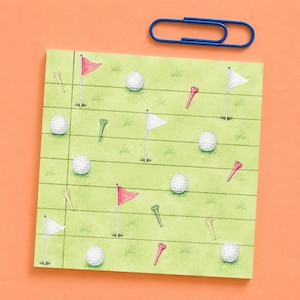 Peut inclure: Un bloc-notes carré avec un fond vert clair présentant un motif répétitif de balles de golf blanches, de drapeaux rouges et blancs et de tees de golf, accompagné d'un trombone bleu placé au-dessus du bloc-notes sur une surface orange.