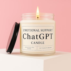 以下が含まれることがあります： 黒い蓋が付いたガラス瓶に入った、火の灯ったキャンドル。ラベルには「EMOTIONAL SUPPORT ChatGPT CANDLE」と書かれています。キャンドルはピンク色の背景の白い表面に置かれています。キャンドルには「natural soy wax candle」と「307 PALMS TO PEACHES」と書かれています。