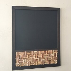May include: A black framed chalkboard with a cork border. The cork border is made up of wine corks with labels.
