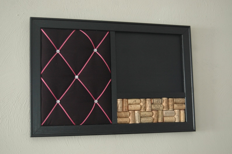 Puede incluir: Un tablero de corcho negro enmarcado con una secci&oacute;n de tela capiton&eacute;, una secci&oacute;n de pizarra y una secci&oacute;n inferior cubierta de corchos de vino. La secci&oacute;n de tela tiene una cinta rosa y diamantes de imitaci&oacute;n.