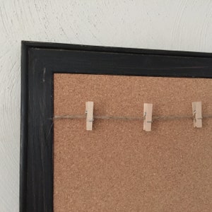 Puede incluir: Un tablero de corcho enmarcado en negro con una cuerda y cuatro pinzas de madera.