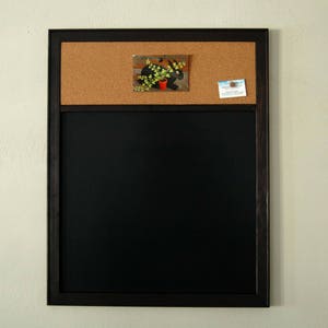 May include: A dark brown framed corkboard with a black chalkboard underneath. The corkboard has a small picture of a plant and a business card attached to it.