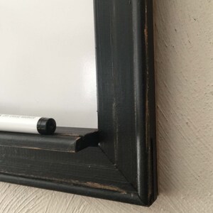 Może przedstawiać: Czarna drewniana rama z białą tablicą do pisania suchą kredą i białym markerem do pisania suchą kredą. Rama ma postarzony wygląd.