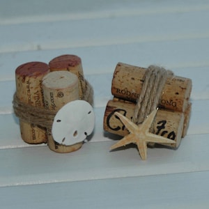 May include: Two small stacks of wine corks decorated with twine, seashells, and a starfish. The corks are tied together with twine and have the words "wood vine" and "Rodney Strong" printed on them.