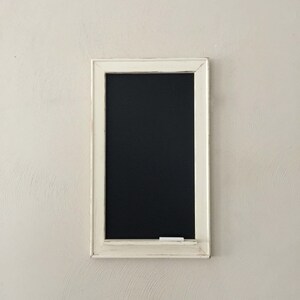 Może przedstawiać: Czarna tablica z białą ramą, z czarną powierzchnią i kawałkiem białej kredy na dolnej krawędzi.