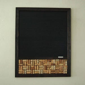 May include: A black framed chalkboard with a cork border made of wine corks. The chalkboard is blank and ready to be written on.