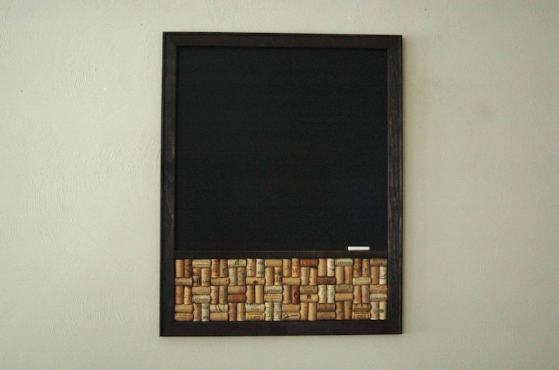 May include: A black framed chalkboard with a cork border made of wine corks. The chalkboard is blank and ready to be written on.