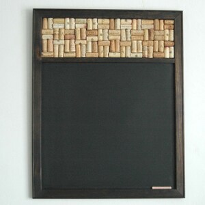 May include: A black chalkboard with a wooden frame and a cork border. The cork border is made of wine corks arranged in a mosaic pattern.