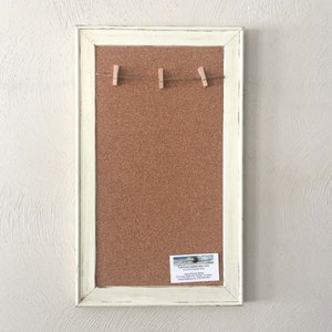 Puede incluir: Un tablero de corcho blanco enmarcado con una cuerda de pinzas para la ropa colgando en la parte superior. El tablero de corcho est&aacute; en blanco y listo para usar. Una tarjeta de visita est&aacute; unida a la esquina inferior derecha del tablero de corcho.