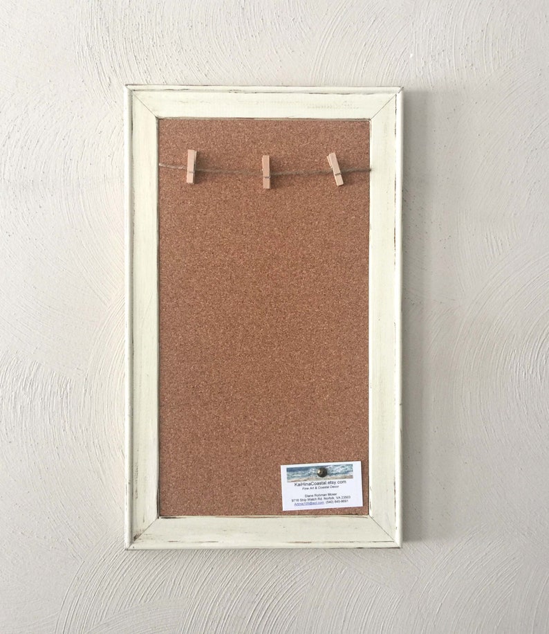 Puede incluir: Un tablero de corcho blanco enmarcado con una cuerda de pinzas para la ropa colgando en la parte superior. El tablero de corcho est&aacute; en blanco y listo para usar. Una tarjeta de visita est&aacute; unida a la esquina inferior derecha del tablero de corcho.