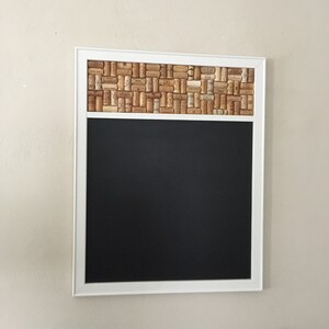 May include: A white framed chalkboard with a cork border made of wine corks. The chalkboard is blank.