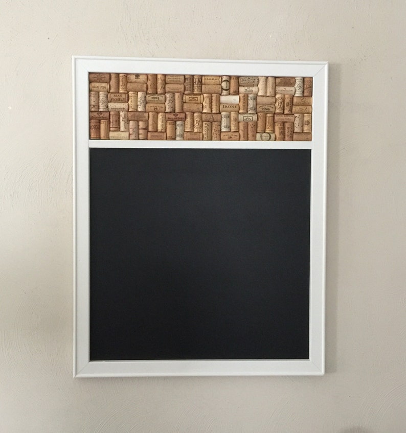 May include: A white framed chalkboard with a cork border. The cork border is made of wine corks and has a variety of labels and text.