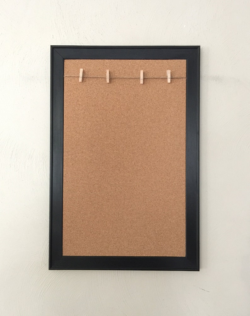 Puede incluir: Un tablero de corcho enmarcado en negro con una cuerda de pinzas para la ropa en la parte superior. El tablero de corcho est&aacute; en blanco y listo para notas o fotos.