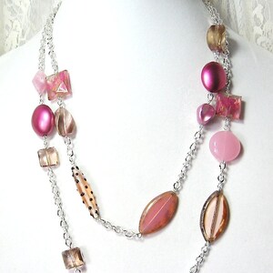 May include: A silver chain necklace with pink and brown beads. The necklace has a layered design with multiple strands of chain and various shapes and sizes of beads.