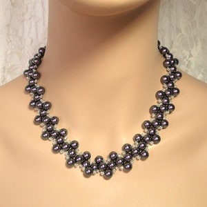 May include: A dark gray pearl necklace with a delicate, intricate design. The necklace is made with small, round pearls and features a repeating pattern of small, clear beads.