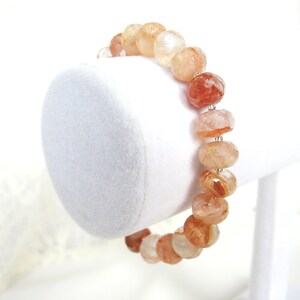 May include: A bracelet made with faceted, translucent, orange and white gemstone beads. The beads are strung on a silver wire.