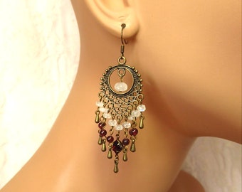 May include: Bronze dangle earrings with a filigree design, featuring white moonstone beads and red garnet beads.