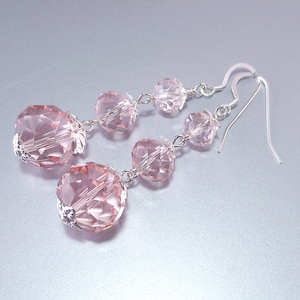 May include: Pink crystal dangle earrings with silver hooks. The earrings feature three faceted crystal beads on each side.