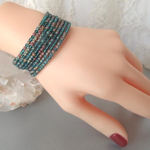 May include: A multi-strand bracelet made of small, teal-colored glass beads. The beads have a subtle iridescent shimmer.