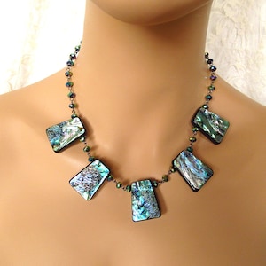May include: A necklace with a silver chain and iridescent abalone shell pendants. The necklace is on a mannequin's neck.