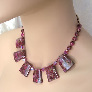 May include: A pink and gold necklace with a geometric pattern. The necklace is made of small round beads and larger rectangular beads. The rectangular beads are a deep pink with gold flecks.