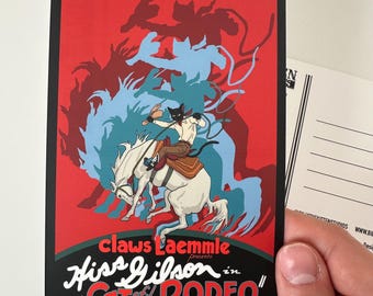 May include: A vintage-style postcard featuring a cat riding a horse in a rodeo scene. The artwork has a red and blue color scheme with the text "Claws Laemmle presents Hiss Gilson in 'Cat of the Rodeo'". The postcard is held by a hand.