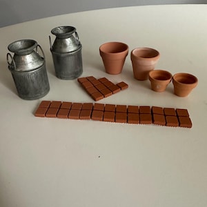 May include: Two miniature silver-colored metal milk cans, four terracotta-colored clay flower pots of varying sizes, and a collection of small, square, flat terracotta-colored tiles arranged in a long row and a separate triangular cluster.