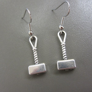 May include: Silver earrings with a hammer charm. The hammer has a twisted handle and a square head.