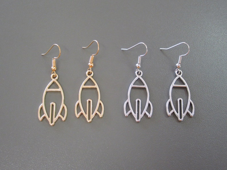 Pu&ograve; includere: Due paia di orecchini a forma di razzo. Un paio &egrave; color oro, l'altro &egrave; color argento. Ogni orecchino ha un gancio per orecchie forate. Gli orecchini sono esposti su uno sfondo grigio.