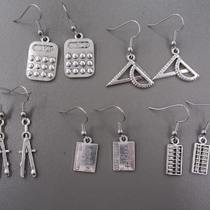 May include: Silver-coloured earrings featuring school-themed charms. Designs include calculators, protractors, compasses, rulers with the fraction 2 2/4, and abacuses. The earrings hang from silver-coloured ear wires.
