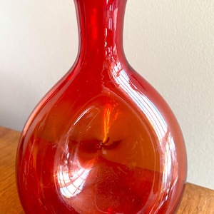 May include: A red glass vase with a round body and a narrow neck. The vase is made of clear glass with a red tint.