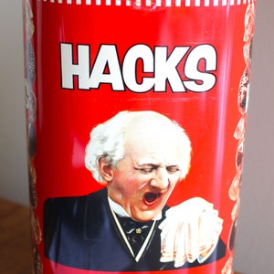Peut inclure: Boîte en métal rouge et blanche avec le mot "Hacks" en lettres blanches. La boîte représente un homme avec une barbe et une moustache blanches, portant un costume noir et un mouchoir blanc. Le texte "Sole Manufacturers White Hudson & Co. Ltd. Southport England" est imprimé sur la boîte.
