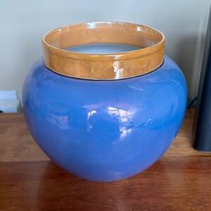 Peut inclure: Un vase en céramique bleu avec un bord brun. Le vase a une finition brillante et est de forme ronde.