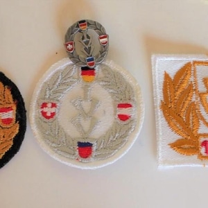 Peut inclure: Ensemble de badges et écussons militaires brodés. Les badges sont circulaires avec un emblème central et des drapeaux. Les écussons comportent les inscriptions "1000 km" et "500 km".
