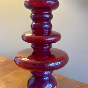 Peut inclure: Un vase en verre rouge haut avec un design unique et superposé. Le vase a une base large et un col étroit, avec trois couches distinctes de verre arrondi.