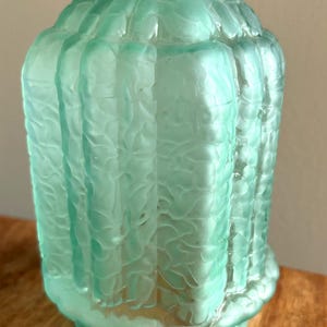 May include: A cylindrical light fixture shade made of frosted mint green glass. The exterior surface features a repeating vertical ribbed pattern with a textured, organic, and wavy finish throughout the glass, creating a semi-translucent appearance.