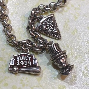 May include: A silver charm bracelet with three detailed charms. One charm is a baseball bat with the text "BUILT 1914". Another charm is a slice of pizza with heart-shaped cutouts. The third charm is a bust of a man wearing a top hat.