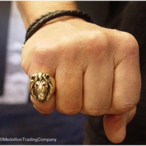 Puede incluir: Un anillo de oro con un diseño de cabeza de león. Los ojos del león están engastados con piedras rojas.
