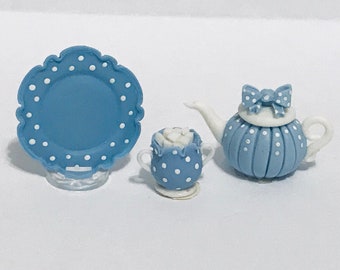 May include: A miniature blue and white polka dot tea set. The set includes a scalloped-edge plate, a teacup, and a teapot with a bow on top. The teapot and teacup have vertical lines. The plate, teacup, and teapot are all blue with white polka dots.