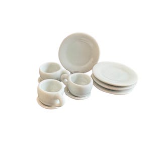 May include: A miniature white ceramic tea set, comprising two teacups with saucers and several small plates. The set is arranged on a white surface, ideal for a doll's house or decorative display.