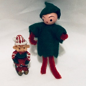 May include: Two Christmas elves, one is a small red and white elf with a candy cane design, the other is a larger green elf with a red and white striped hat and red pipe cleaner legs.