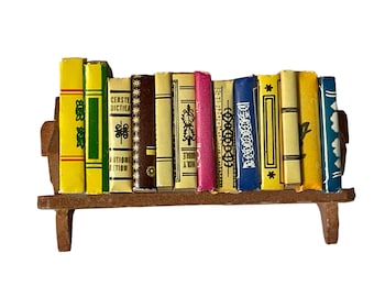 May include: A miniature wooden bookshelf with a row of colorful books. The books have various titles and designs, including "Bible Book", "Cersten Diction", and "A Holy Guide".