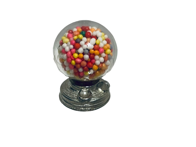 May include: A miniature gumball machine with a clear, round globe filled with colorful gumballs. The base is silver-colored with a classic design. A small, nostalgic candy dispenser.