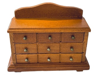 May include: A wooden dresser with 12 drawers and a curved top. The dresser is made of light brown wood and has brass knobs on the drawers.