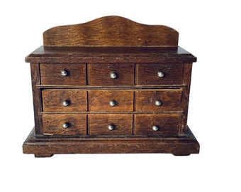 May include: A wooden dresser with nine drawers, each with a silver knob. The dresser has a dark brown finish and a slightly curved top.