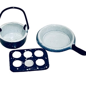 May include: A set of three miniature kitchen cookware items in white and black. The set includes a small pot with a handle, a frying pan, and a muffin tin.