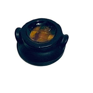 May include: A small black cauldron with two handles, filled with a golden liquid. The cauldron is made of a smooth, dark material and has a slightly rounded shape.