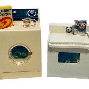 Peut inclure: Ensemble de jouets miniatures : une machine &agrave; laver et un s&egrave;che-linge. La machine &agrave; laver est blanc cass&eacute; avec une porte transparente et un objet vert &agrave; l'int&eacute;rieur. Une bo&icirc;te de "LAUNDRY DETERGENT" est pos&eacute;e dessus. Le s&egrave;che-linge est blanc cass&eacute; avec une bo&icirc;te de d&eacute;tergent "Rinso".